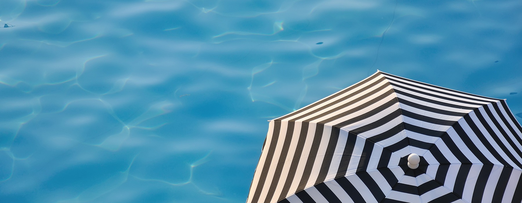 lifestyle image of an umbrella beside a sparkling swimming pool